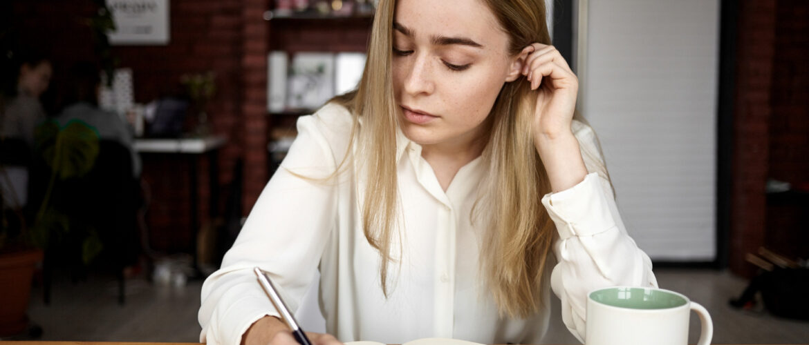 An attractive blonde student girl in a white blouse doing homework